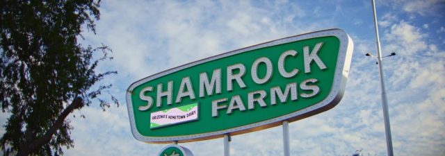 Large green Shamrock Farms road sign reading "Arizona's Hometown Dairy" against a blue sky with clouds, captured during branded documentary production by NewLeaf Production Group